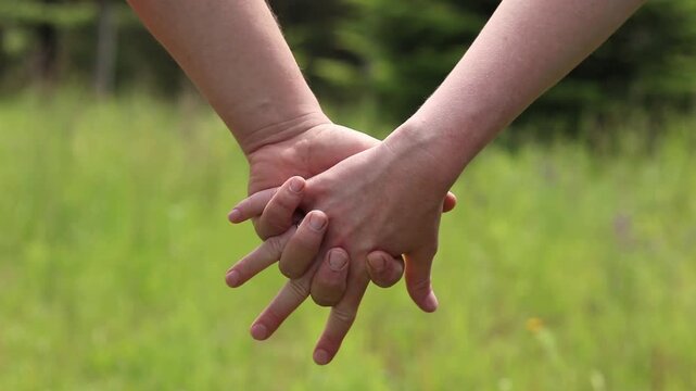 Couple holding hands on nature background. Close-up of hands of man and woman intertwined with fingers during a walk in the fresh air. Concept of love, support and unity. Two people holding hands