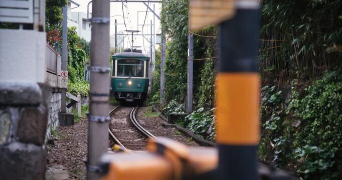 Japanese tram approaching gate surrounded by village brush - steady cam shot