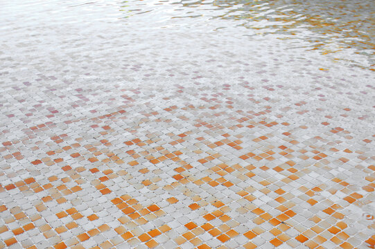 Water surface with colorful ceramic tiles seen on the bottom of a swimming pool.