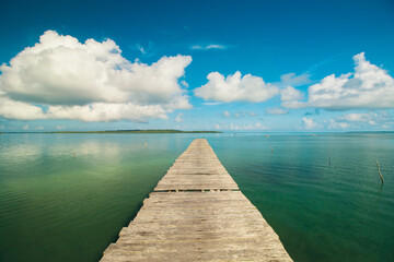 Fototapeta premium Tranquil wooden pier extending into calm tropical sea under blue sky