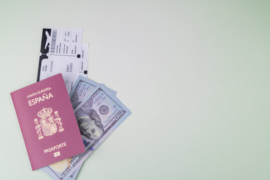 Sleek red Spain passport with airplane flight tickets and hundred dollar bills inside on a green and cream gradient background