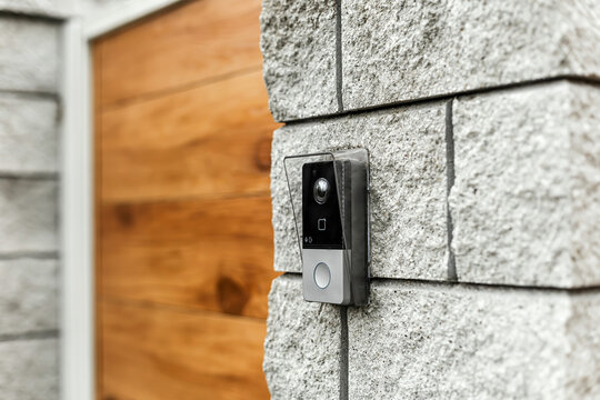 Smart video doorbell camera mounted on a modern stone wall entrance. Home security concept.