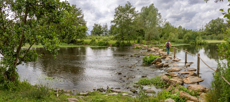 Woman crossing a stream in Molenplas protected area near Stevensweert, part of the Maas valley river park on the Netherlands Belgium border. 