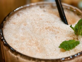 High angle close up of creamy frothy drink foam garnished with fresh green mint leaves and a black straw in a glass. © EkoPriyatno
