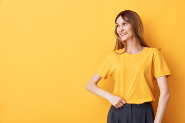 Obraz premium Young woman in a yellow shirt smiles softly against a vivid yellow backdrop, creating a warm casual portrait ideal for lifestyle and fashion projects