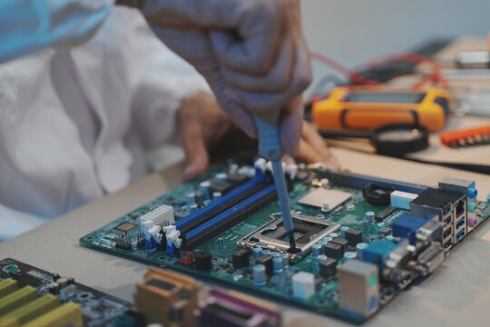 A technician's gloved hand works with a screwdriver on a motherboard CPU socket area, shown from an eye-level perspective. Dismantled hard drives .