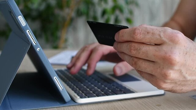 Person pays online with credit card beside tablet keyboard for secure shopping and digital banking at modern home work desk