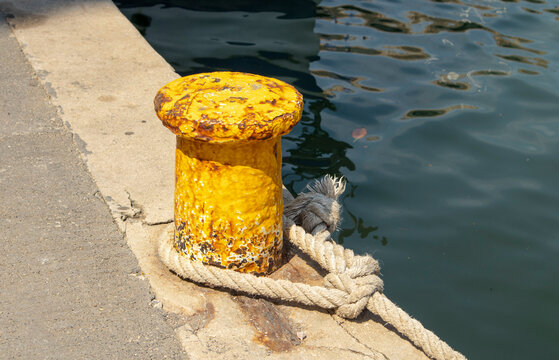 Weathered yellow mooring bollard with thick rope tied on concrete pier at seaside fishing harbor