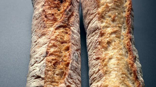 Two Rustic Baguettes on Dark Surface. Close-up of two rustic baguettes with golden crispy crust and flour dusting on a dark surface. Artisan French bread bakery background.