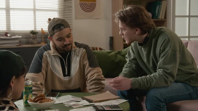Diverse young flatmates sitting at coffee table, discussing bills, counting cash, planning domestic expenses and calculating budget. Personal finance apps or student banking advertisements