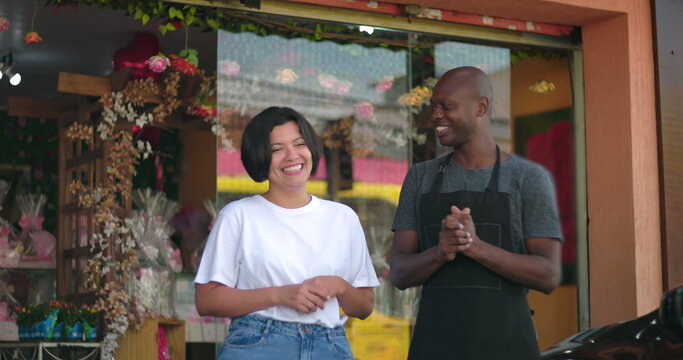 Two small business owners laughing together outside flower shop, joyful interaction and positive energy, floral background and friendly atmosphere