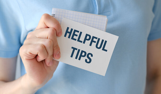 Hand holds note with bold text: HELPFUL TIPS. Person wears light blue shirt, shows note clearly. Image conveys guidance, advice, or useful information.