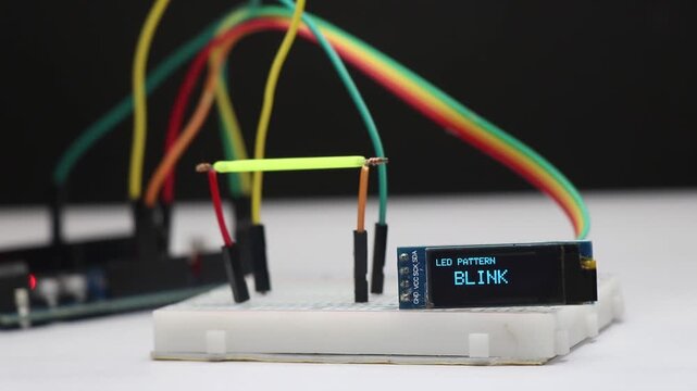 Breadboard electronics circuit with LED filament showing blink, fade, and pulse light patterns, controlled by microcontroller in the background