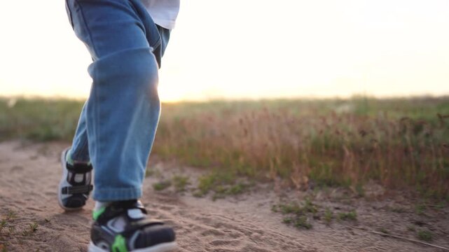 A boy is running along a dirt path in the fields. His blue pants and shoes are notable as he moves swiftly through the open space.