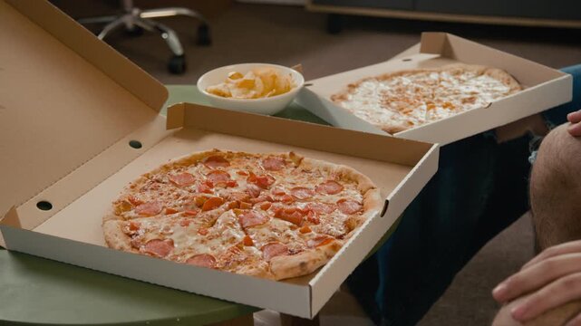 Young man opening pizza delivery box on table and checking receipt while sharing fast food meal with flatmates at dorm. Delivery apps, college student budget lifestyle, or cheap eats promotions
