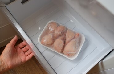Raw chicken legs in the freezer. A hand opens the freezer compartment, revealing a package of frozen chicken drumsticks © LineDP