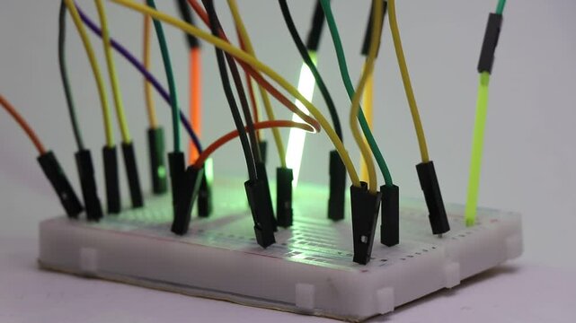Close up view of glowing LED filament tube lights connected to breadboard with jumper cables illuminating in sequential order