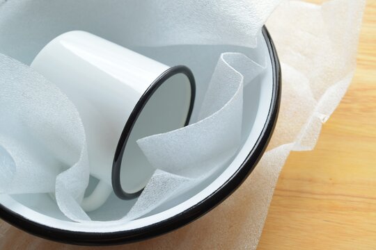 New enamelware on a wooden table. Enameled bowl and mug in wrapping paper