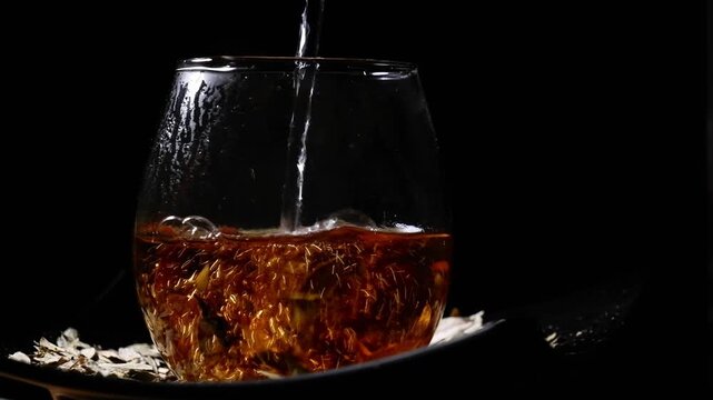 Hot water pouring into glass cup with dried senna leaves on table for herbal infusion concept