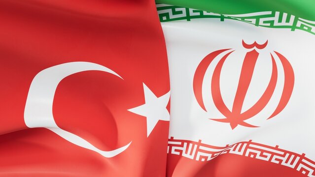 This image shows the flags of T&uuml;rkiye and Iran waving side by side, symbolizing their brotherly ties, political solidarity, and strategic partnership between the two countries.