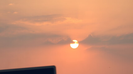 Fototapeta premium Dreamy orange sunset with glowing sunlight and layered clouds creating a relaxing sky view.