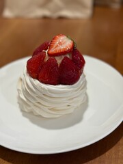 Strawberry pavlova dessert with whipped cream on white plate in cozy indoor setting © dvoevnore