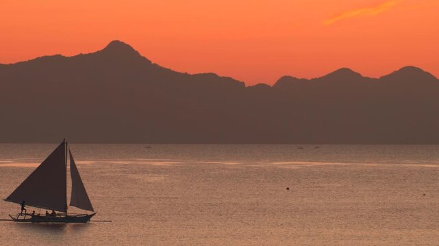 Traditional sailboat crossing calm Philippine waters at orange sunset