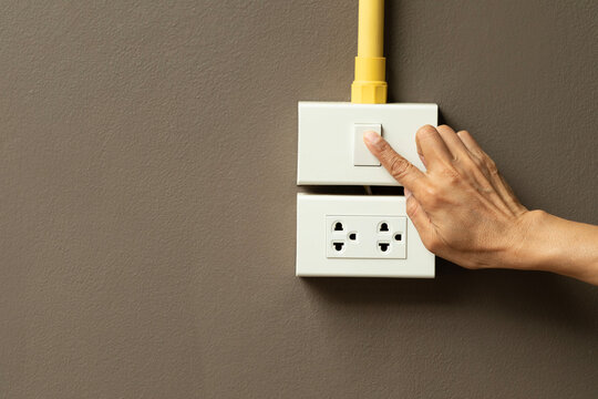 Hand turning on light switch on brown wall