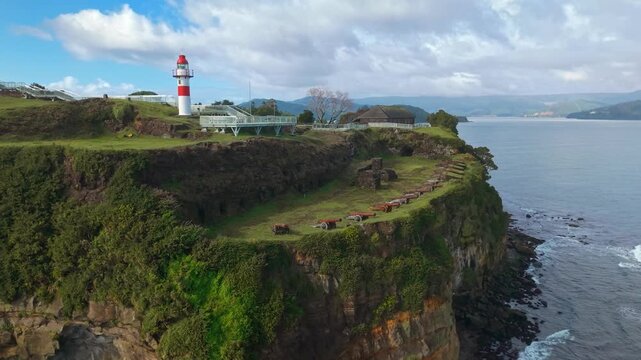 A bird's-eye view of the row of cannons and the red lighthouse at Niebla Castle in Niebla, near Valdivia, Chile, on a sunny day, with the Valdivia River in the background