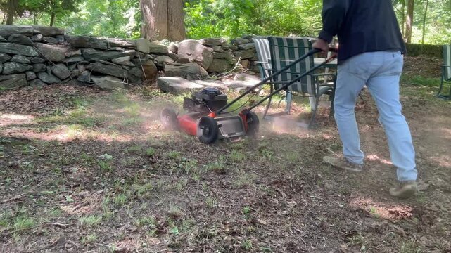 Rear view tracking shot of person mowing patchy backyard dirt