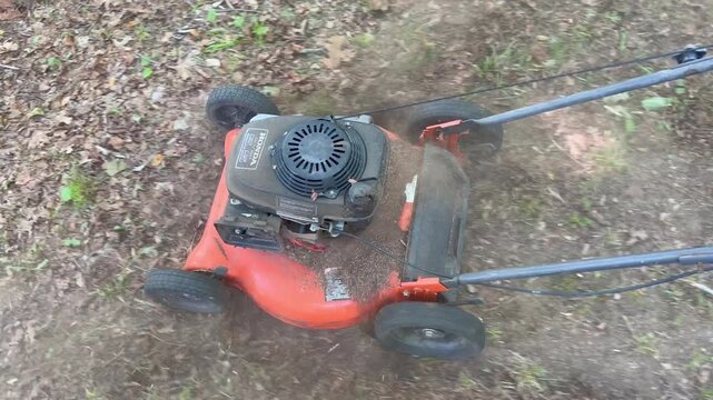 Top view of push lawnmower operating on patchy backyard grass