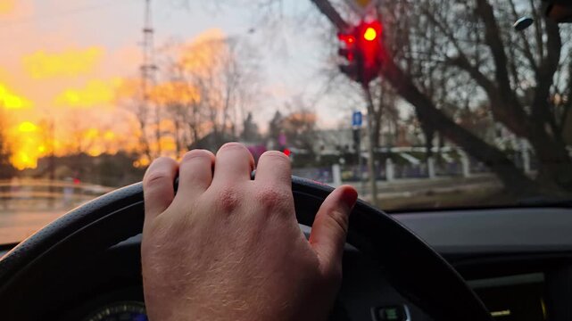 Anxious commuter grips wheel beside glowing stoplight beneath vivid sunset glow