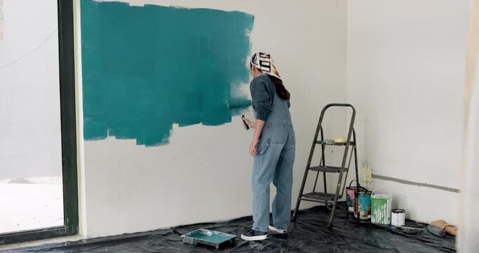 Woman, roller and painting in home with renovation project, interior design and property makeover. Back, creative person and art tools in living room with house improvement, diy or remodeling process