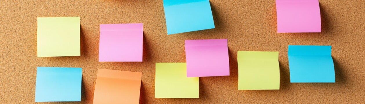Brightly colored blank sticky notes scattered on a textured cork board, symbolizing ideas, reminders, or a creative project. Planning, productivity