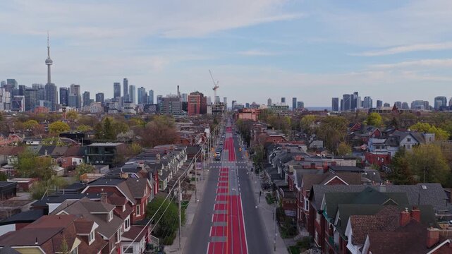 Flying over a red streetcar lane on Shaw Street, Toronto's downtown skyline and CN Tower in background, showcasing urban residential houses