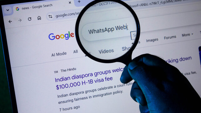 Closeup of a person using a magnifying glass to search for whatsapp web on a computer screen displaying news about h1b visa fees