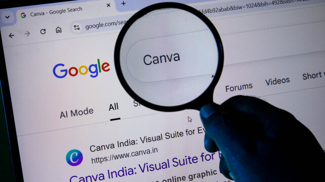 A hand holding a magnifying glass over a computer screen showing a google search result for canva