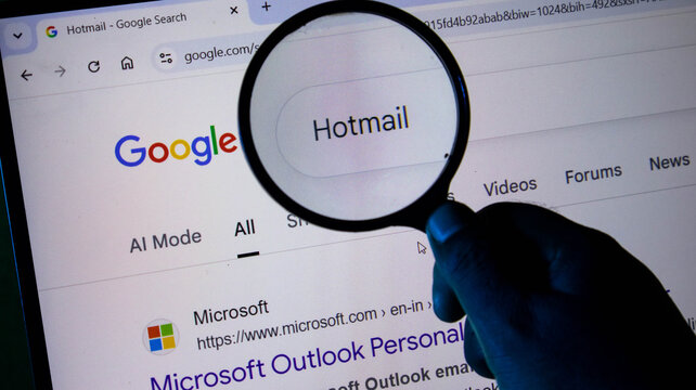 A person using a magnifying glass to search for hotmail on a computer screen showing the google search engine interface