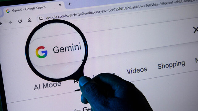 Closeup of a hand holding a magnifying glass over a computer screen displaying the google gemini search results page
