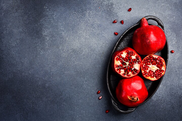 Obraz premium A close-up image of whole pomegranates, open pomegranates, and pomegranate seeds in a bowl. On a concrete background. Top view.
