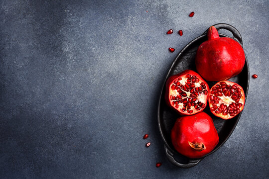 A close-up image of whole pomegranates, open pomegranates, and pomegranate seeds in a bowl. On a concrete background. Top view.