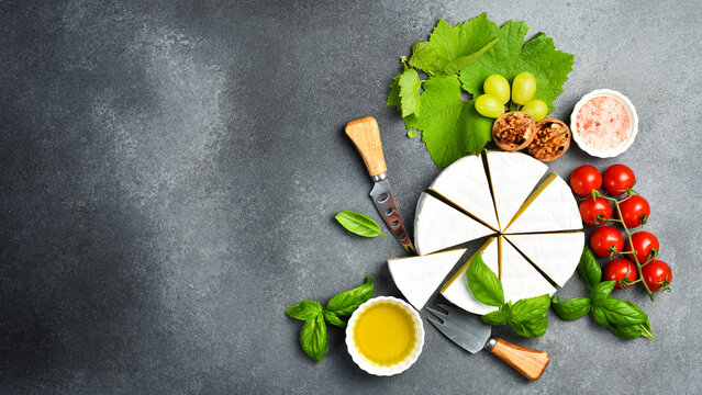 Delicious Brie cheese cut into slices, served with basil and spices. On a stone background. Cold appetizers.