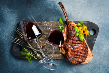 Obraz premium Wine in glasses and a juicy grilled steak on the bone. On a gray concrete background. Free space for text. Top view.