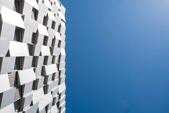 White facade rises against blue sky, with geometric balconies on a building exterior creating pattern, windows, architecture and urban detail
