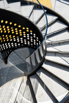 Spiral staircase curves through shadow and light, with metal railing, steps, geometry, interior architecture and circular pattern detail