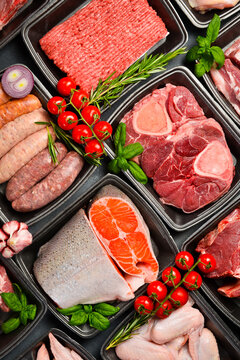 Top view. Set of fresh raw meat and fish. In black plastic containers. Products from the market. Vertical photo.