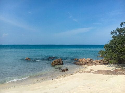 A scenic tropical beach with scattered rocks on the white sand and in the clear blue sea water