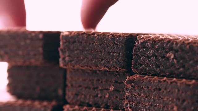 Hand taking crispy waffles with chocolate filling one by one from a stack on white background
