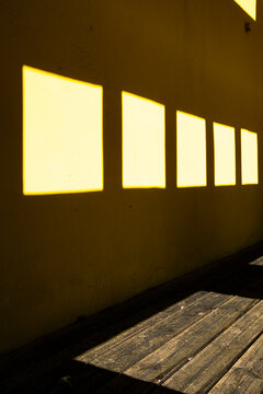 Sharp sunlight turns a yellow wall and wooden floor into pattern, where shadow, window light, courtyard facade and architecture converge