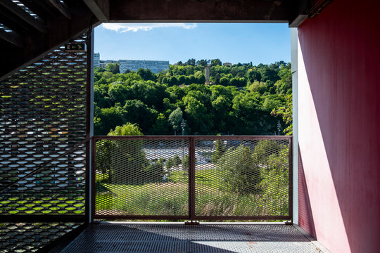 Shaded corridor frames a balcony view toward green trees, where railing, terrace, landscape and building architecture create depth